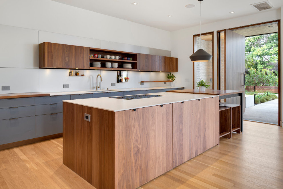 Large contemporary kitchen in Orange County with flat-panel cabinets, dark wood cabinets, solid surface benchtops, metallic splashback, light hardwood floors, with island and white benchtop.