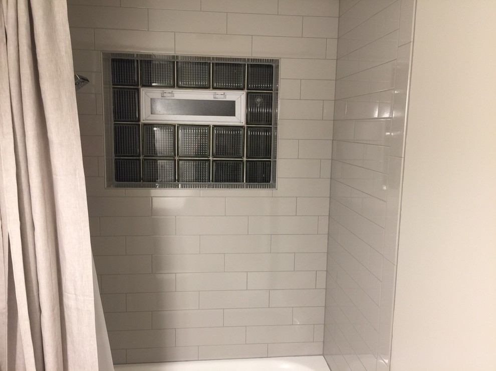 Inspiration for a mid-sized transitional 3/4 bathroom in Chicago with gray tile, porcelain floors, shaker cabinets, grey cabinets, an alcove tub, a shower/bathtub combo, a two-piece toilet, subway tile, grey walls, an undermount sink and solid surface benchtops.