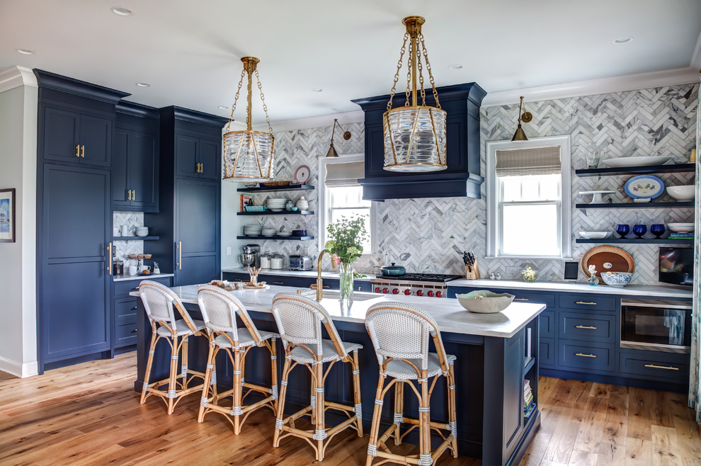 Photo of a large beach style open plan kitchen in New York with an undermount sink, blue cabinets, grey splashback, with island, beaded inset cabinets, marble benchtops, mosaic tile splashback, panelled appliances and light hardwood floors.