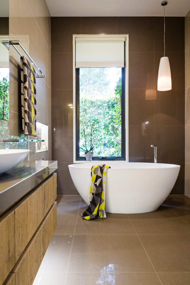 Photo of a mid-sized contemporary master bathroom in Melbourne with flat-panel cabinets, medium wood cabinets, a freestanding tub, an open shower, a wall-mount toilet, beige tile, porcelain tile, beige walls, porcelain floors, a vessel sink, engineered quartz benchtops, brown floor, an open shower and brown benchtops.