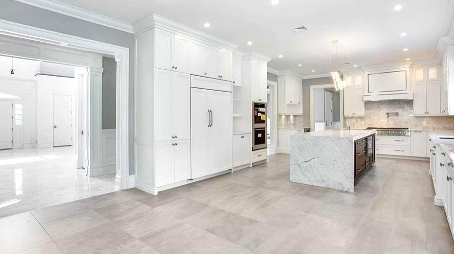 This is an example of an expansive transitional galley eat-in kitchen in New York with a drop-in sink, shaker cabinets, white cabinets, quartzite benchtops, multi-coloured splashback, ceramic splashback, panelled appliances, ceramic floors, with island, beige floor and white benchtop.