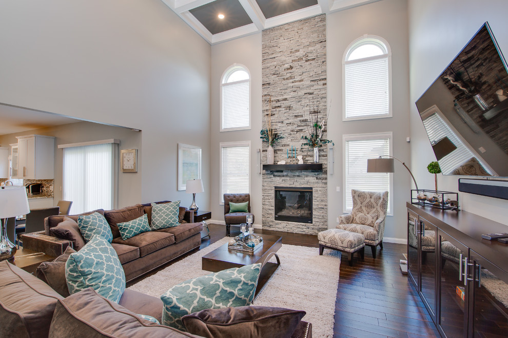 Inspiration for a large transitional open concept family room in Grand Rapids with grey walls, dark hardwood floors, a standard fireplace, a stone fireplace surround, a wall-mounted tv and brown floor.