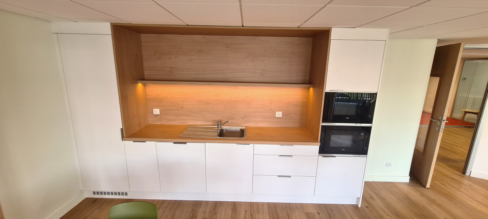 Small modern single-wall open plan kitchen in Lille with an undermount sink, beaded inset cabinets, white cabinets, wood benchtops, brown splashback, timber splashback, stainless steel appliances, medium hardwood floors, no island, brown floor and brown benchtop.