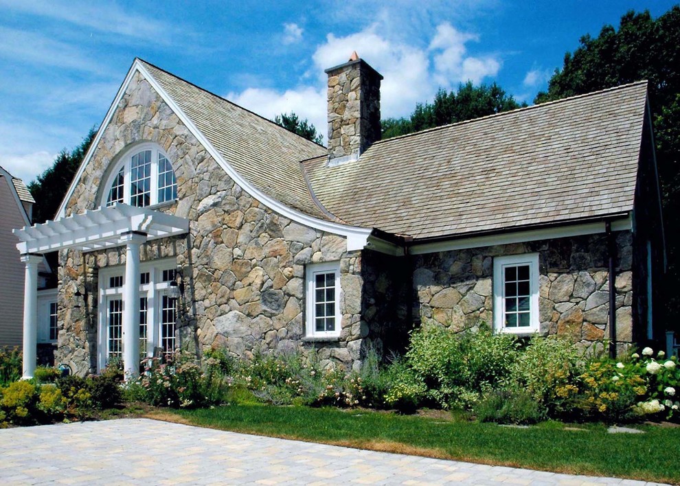 This is an example of a mid-sized traditional two-storey beige house exterior in Boston with stone veneer, a gable roof and a shingle roof.