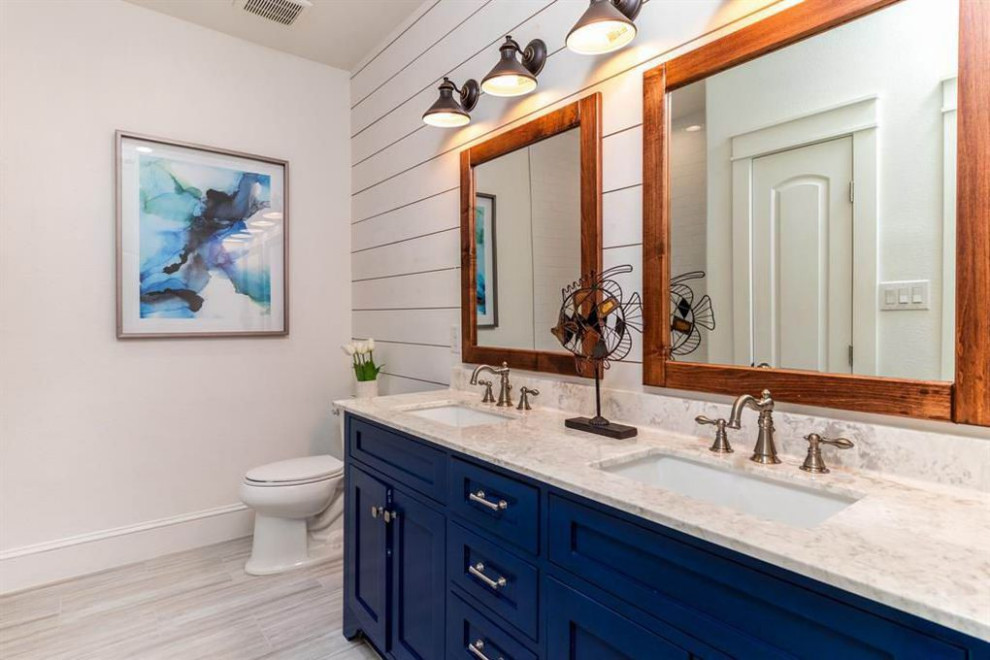 Design ideas for a beach style bathroom in Houston with shaker cabinets, blue cabinets, a drop-in tub, a shower/bathtub combo, a one-piece toilet, white tile, ceramic tile, white walls, ceramic floors, an undermount sink, marble benchtops, grey floor and white benchtops.