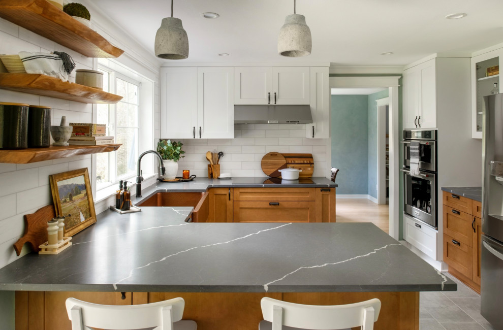 This is an example of a medium sized traditional u-shaped kitchen/diner in Seattle with a belfast sink, shaker cabinets, medium wood cabinets, engineered stone countertops, white splashback, marble splashback, stainless steel appliances, ceramic flooring, a breakfast bar, grey floors and grey worktops.