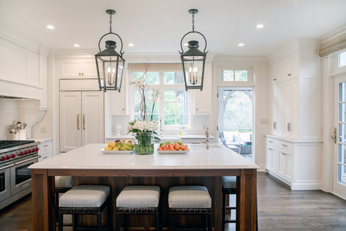 Bright white kitchen with shaker kitchen cabinet wall, marble-top island, black lantern pendants, and four upholstered stools.