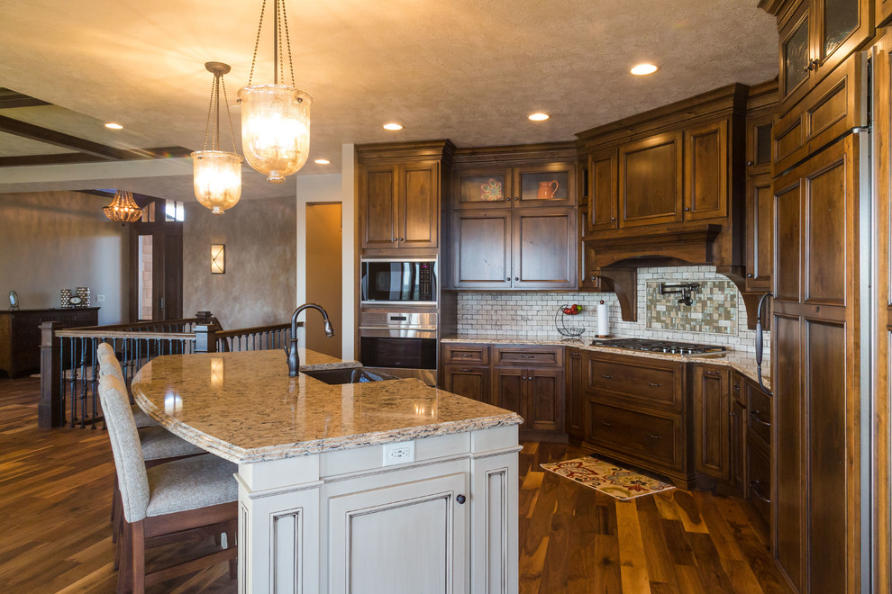Mid-sized transitional l-shaped medium tone wood floor eat-in kitchen photo with a farmhouse sink, recessed-panel cabinets, medium tone wood cabinets, granite countertops, beige backsplash, stone tile backsplash, stainless steel appliances and an island
