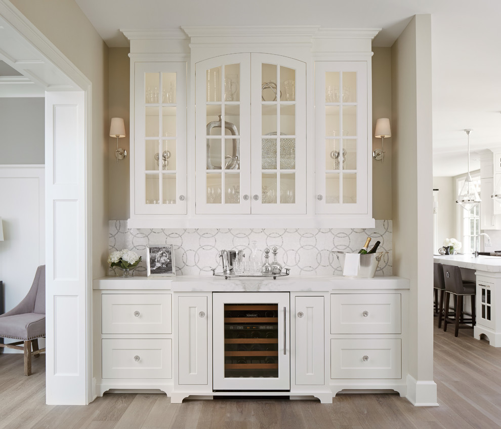 This is an example of a large contemporary single-wall wet bar in Chicago with recessed-panel cabinets, white cabinets, white splashback, mosaic tile splashback, light hardwood floors, no sink and white benchtop.