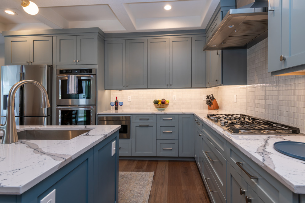 Inspiration for a mid-sized transitional u-shaped laminate floor, brown floor and coffered ceiling eat-in kitchen remodel in Denver with an undermount sink, shaker cabinets, blue cabinets, quartz countertops, white backsplash, ceramic backsplash, stainless steel appliances, an island and white countertops
