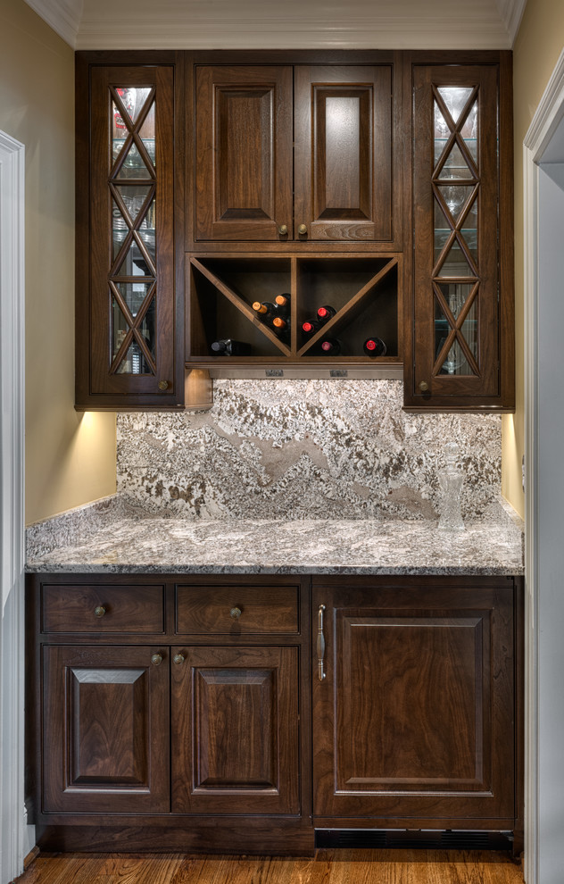 Inspiration for a small traditional single-wall wet bar in Other with raised-panel cabinets, granite benchtops, no sink, dark wood cabinets, grey splashback, stone slab splashback, medium hardwood floors and grey benchtop.