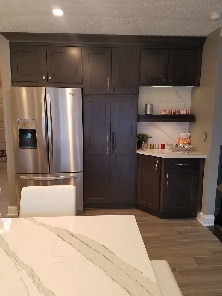 Inspiration for a mid-sized transitional l-shaped porcelain tile and gray floor enclosed kitchen remodel with an undermount sink, raised-panel cabinets, dark wood cabinets, quartz countertops, white backsplash, stone slab backsplash, stainless steel appliances and an island