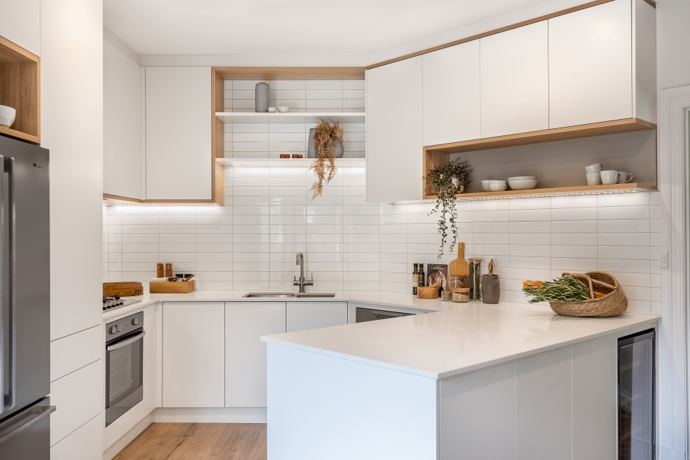 Inspiration for a small contemporary u-shaped eat-in kitchen in Adelaide with an undermount sink, flat-panel cabinets, white cabinets, quartz benchtops, white splashback, subway tile splashback, stainless steel appliances, laminate floors, a peninsula, brown floor and white benchtop.