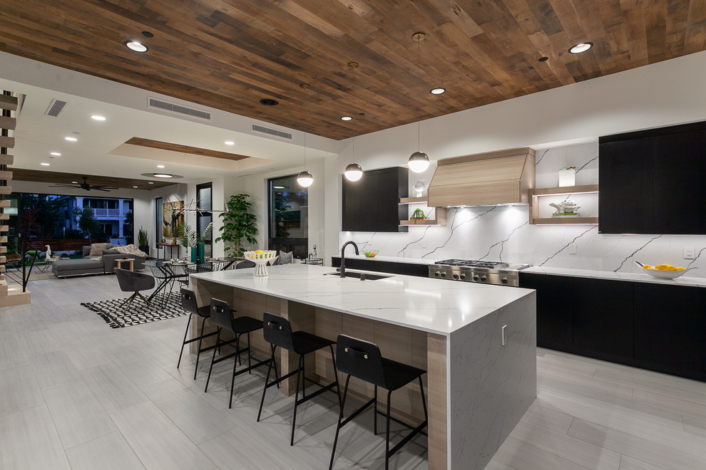 Inspiration for a contemporary single-wall open plan kitchen in Orange County with an undermount sink, flat-panel cabinets, black cabinets, white splashback, stainless steel appliances, with island, beige floor and white benchtop.