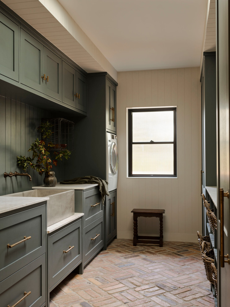 Design ideas for an expansive transitional galley dedicated laundry room in Sydney with shaker cabinets, a stacked washer and dryer, a farmhouse sink, grey cabinets, beige walls, brick floors, red floor, white benchtop and planked wall panelling.