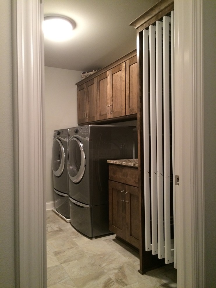 This is an example of a small traditional single-wall laundry room in Milwaukee with an utility sink, granite benchtops, grey walls, ceramic floors, a side-by-side washer and dryer, recessed-panel cabinets and dark wood cabinets.
