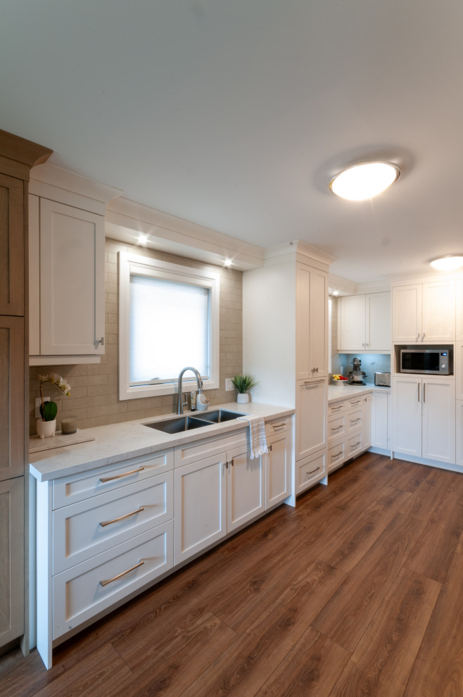 Example of a mid-sized transitional galley laminate floor and brown floor eat-in kitchen design in Toronto with an undermount sink, recessed-panel cabinets, white cabinets, quartz countertops, beige backsplash, porcelain backsplash, stainless steel appliances and yellow countertops