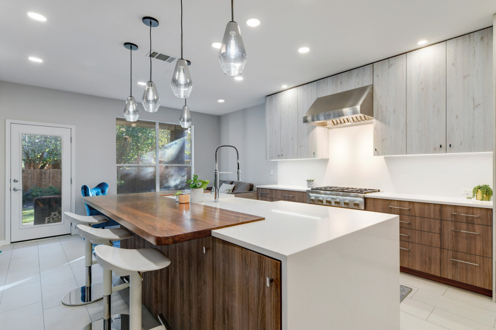 Photo of a large transitional l-shaped open plan kitchen in Austin with a farmhouse sink, flat-panel cabinets, light wood cabinets, quartz benchtops, white splashback, engineered quartz splashback, stainless steel appliances, ceramic floors, with island, grey floor and white benchtop.