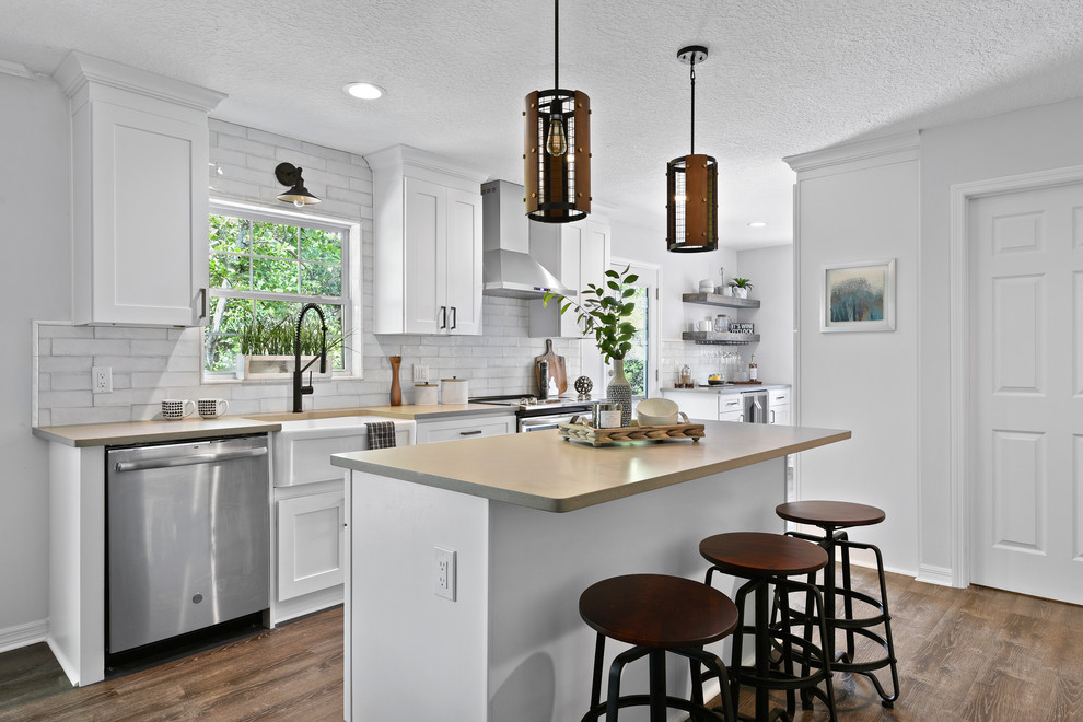 Photo of a country galley eat-in kitchen in Jacksonville with a farmhouse sink, shaker cabinets, white cabinets, white splashback, stainless steel appliances, medium hardwood floors, with island, brown floor and grey benchtop.