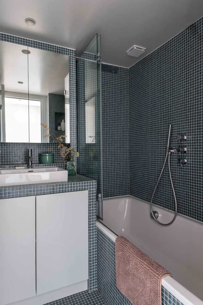 Small contemporary master bathroom in Paris with beaded inset cabinets, blue cabinets, an undermount tub, blue tile, glass tile, blue walls, mosaic tile floors, a drop-in sink, tile benchtops, blue floor and blue benchtops.