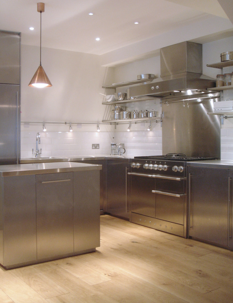 Inspiration for a mid-sized contemporary l-shaped open plan kitchen in London with an integrated sink, flat-panel cabinets, stainless steel cabinets, stainless steel benchtops, white splashback, cement tile splashback, stainless steel appliances, light hardwood floors, with island and beige floor.