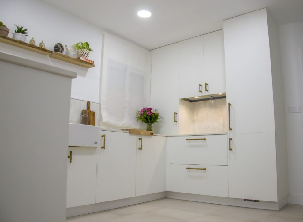 This is an example of a medium sized bohemian u-shaped open plan kitchen in Malaga with a belfast sink, white cabinets, white appliances, a breakfast bar and white floors.