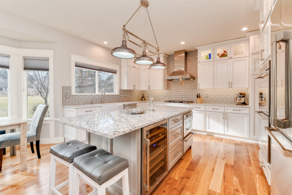 Example of a mid-sized transitional u-shaped medium tone wood floor and brown floor eat-in kitchen design in Boise with a farmhouse sink, shaker cabinets, white cabinets, quartz countertops, gray backsplash, subway tile backsplash, stainless steel appliances and an island