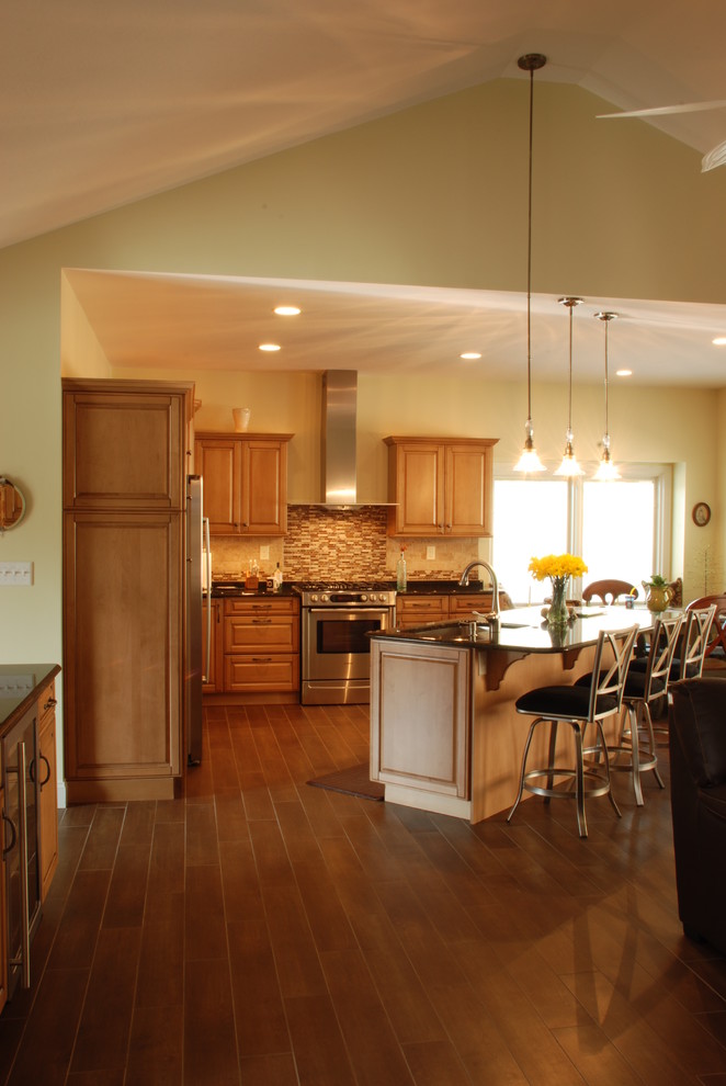 Example of a mid-sized transitional l-shaped ceramic tile eat-in kitchen design with a farmhouse sink, raised-panel cabinets, medium tone wood cabinets, granite countertops, beige backsplash, ceramic backsplash, stainless steel appliances and an island