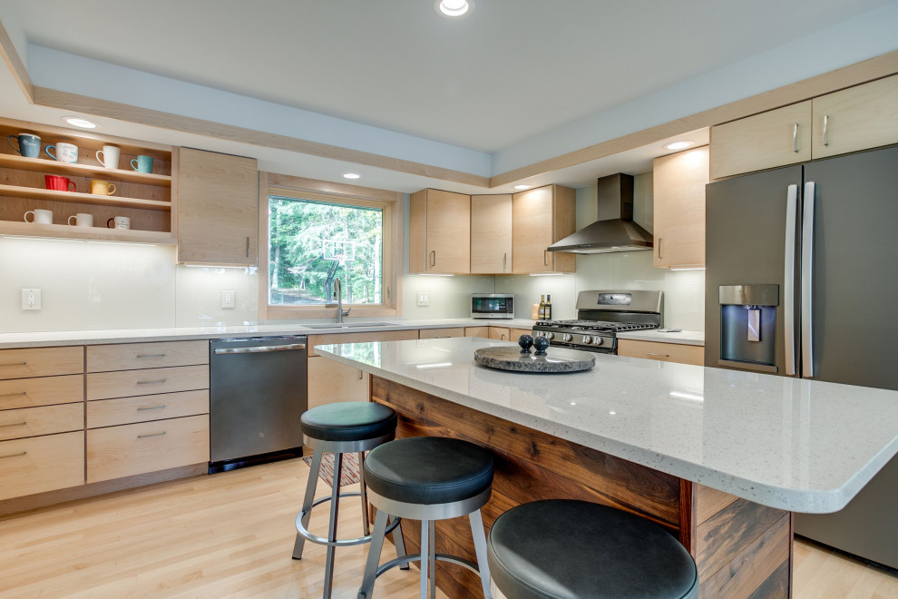Mid-sized mountain style l-shaped light wood floor open concept kitchen photo with a double-bowl sink, flat-panel cabinets, light wood cabinets, quartz countertops, beige backsplash, glass sheet backsplash, stainless steel appliances, an island and white countertops