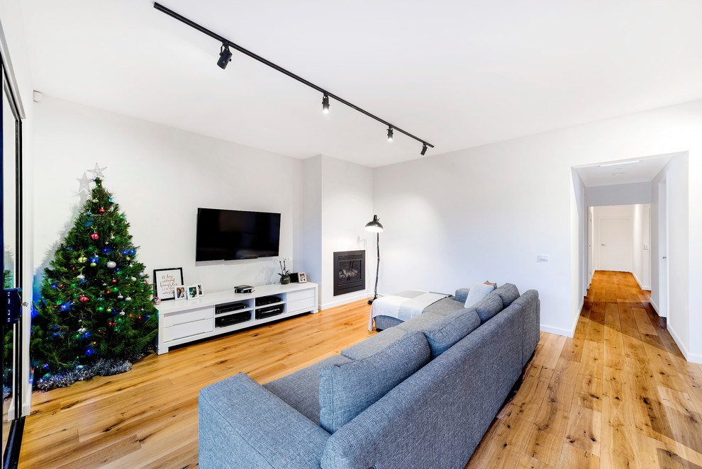 Photo of a mid-sized modern open concept living room in Melbourne with white walls, medium hardwood floors, a hanging fireplace and a wall-mounted tv.