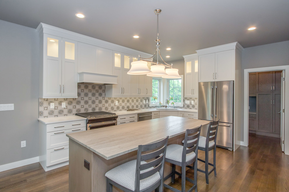Example of a mid-sized transitional l-shaped medium tone wood floor and brown floor eat-in kitchen design in Cedar Rapids with a double-bowl sink, recessed-panel cabinets, white cabinets, quartz countertops, multicolored backsplash, porcelain backsplash, stainless steel appliances, an island and white countertops