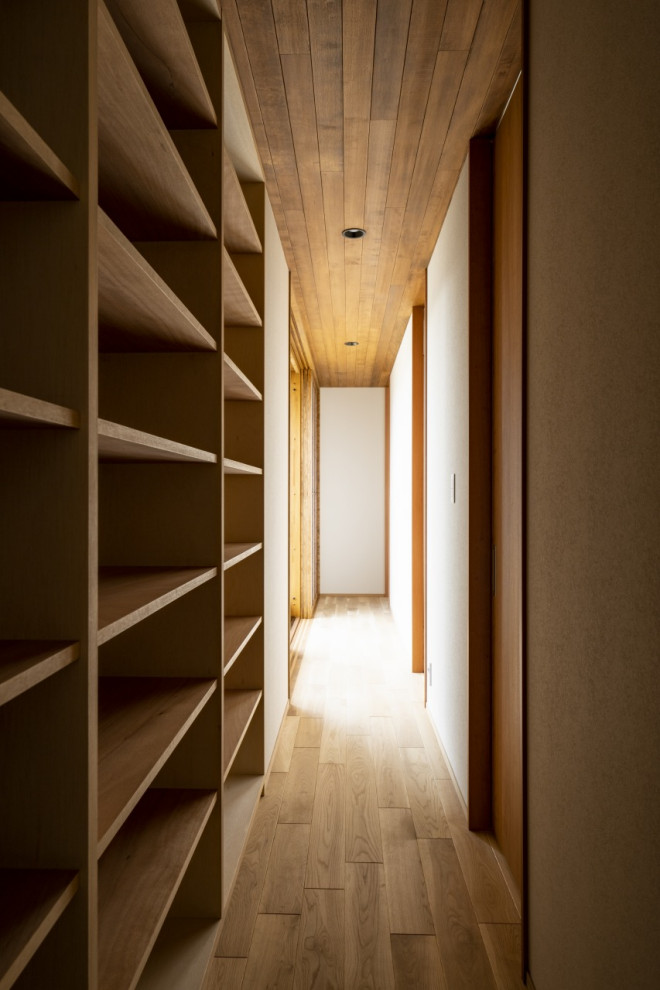 Photo of a mid-sized hallway in Other with white walls, light hardwood floors, brown floor, wood and wallpaper.