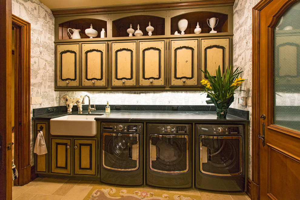 Inspiration for a large traditional galley dedicated laundry room in Santa Barbara with a farmhouse sink, raised-panel cabinets, light wood cabinets, soapstone benchtops, limestone floors and a side-by-side washer and dryer.