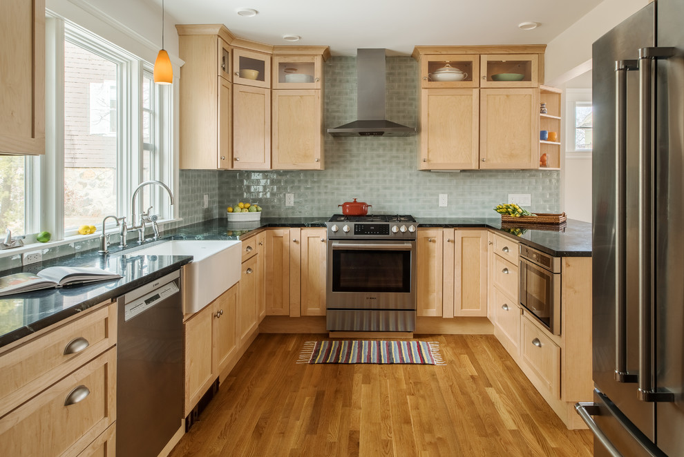This is an example of a transitional u-shaped kitchen in Boston with a farmhouse sink, shaker cabinets, light wood cabinets, green splashback, stainless steel appliances, medium hardwood floors, black benchtop and soapstone benchtops.