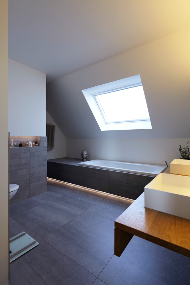 Photo of an expansive scandinavian 3/4 bathroom in Cologne with a vessel sink, a drop-in tub, gray tile, stone tile and white walls.