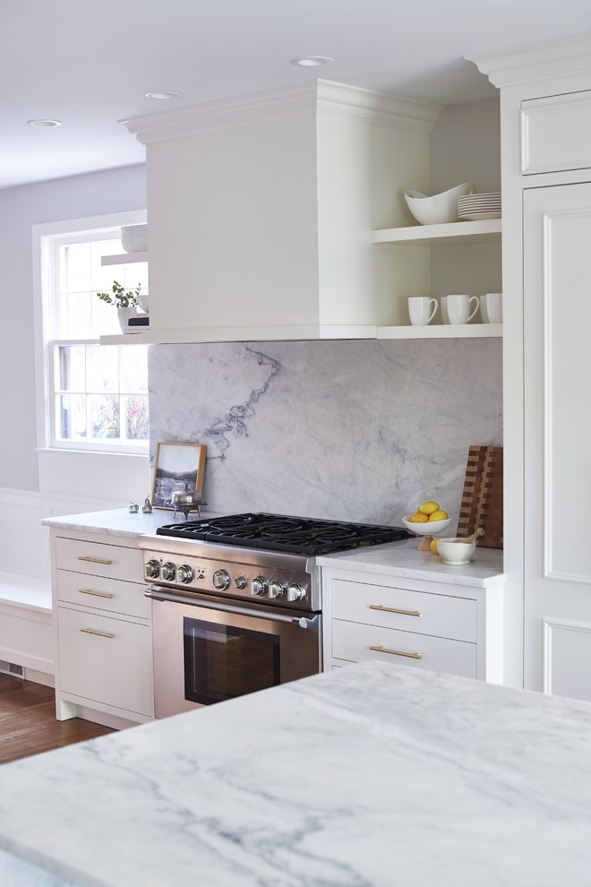 Design ideas for a mid-sized traditional single-wall eat-in kitchen in Cleveland with an undermount sink, flat-panel cabinets, white cabinets, marble benchtops, white splashback, marble splashback, panelled appliances, medium hardwood floors, with island, brown floor and white benchtop.