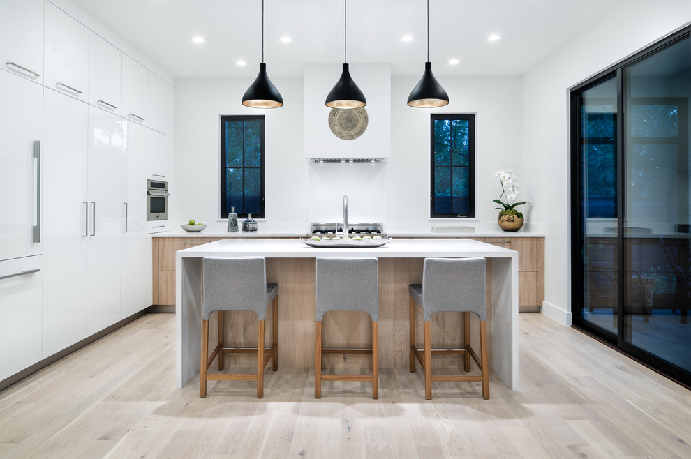 Design ideas for a large country kitchen in Austin with flat-panel cabinets, white cabinets, solid surface benchtops, white splashback, light hardwood floors, with island, beige floor, panelled appliances and white benchtop.