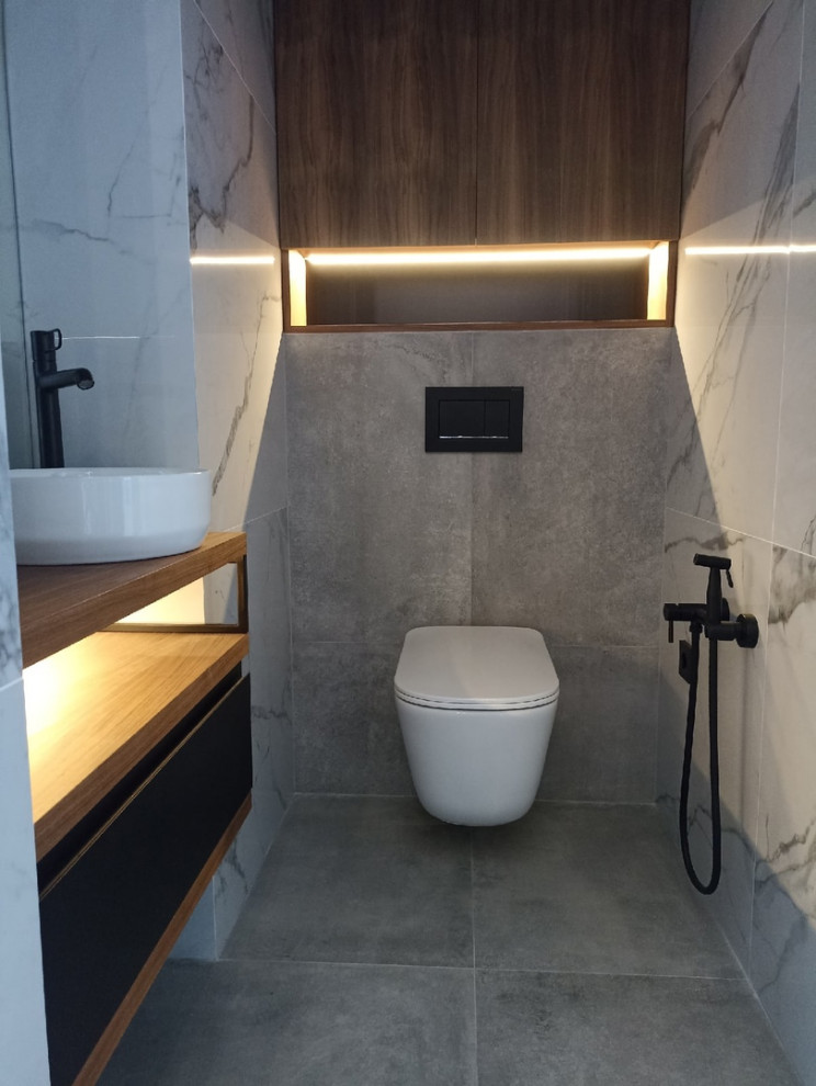 Mid-sized contemporary powder room in Moscow with flat-panel cabinets, brown cabinets, a wall-mount toilet, white tile, ceramic tile, white walls, ceramic floors, a vessel sink, wood benchtops, grey floor, brown benchtops and a floating vanity.