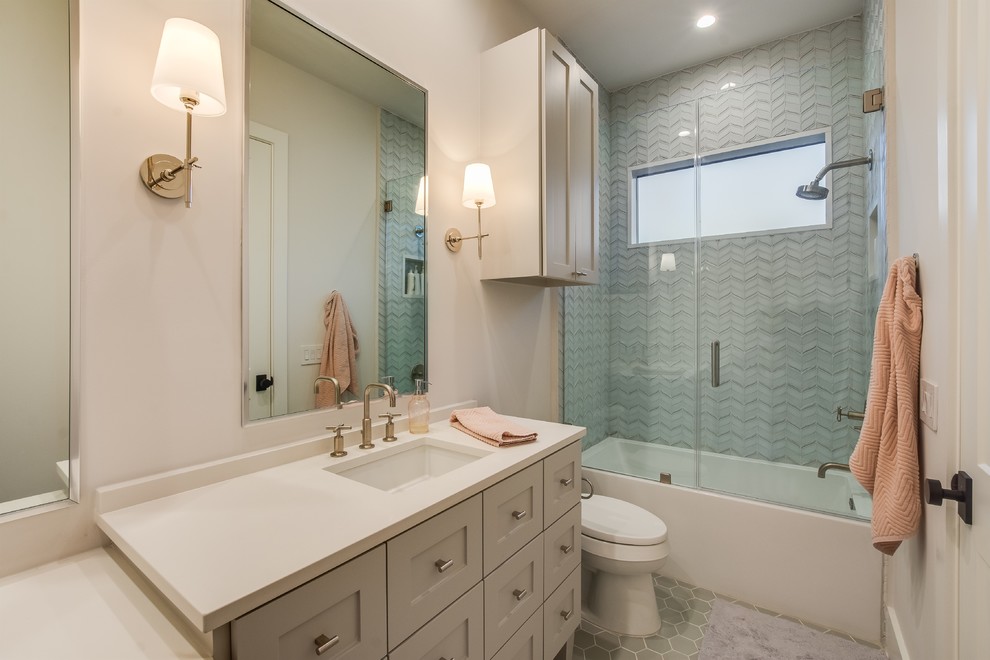 Design ideas for a mid-sized transitional bathroom with shaker cabinets, white cabinets, an alcove tub, a shower/bathtub combo, a one-piece toilet, multi-coloured tile, matchstick tile, white walls, porcelain floors, an undermount sink, engineered quartz benchtops, grey floor, a hinged shower door and white benchtops.