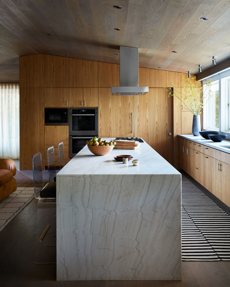 This is an example of a midcentury kitchen in San Francisco with flat-panel cabinets, light wood cabinets, dark hardwood floors, with island, white benchtop, vaulted and wood.