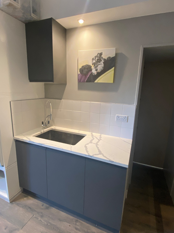 Design ideas for a large contemporary galley utility room in London with a built-in sink, flat-panel cabinets, grey cabinets, quartz worktops, white splashback, porcelain splashback, beige walls, laminate floors, a side by side washer and dryer, grey floors and multicoloured worktops.