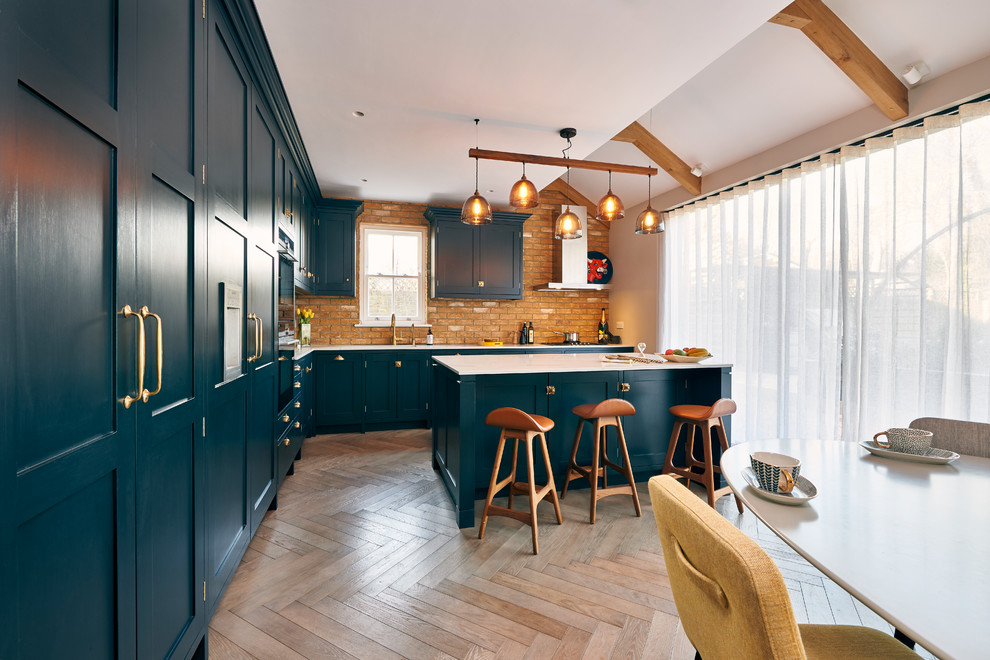 ロンドンにある高級な広いコンテンポラリースタイルのおしゃれなキッチン (シェーカースタイル扉のキャビネット、茶色いキッチンパネル、レンガのキッチンパネル、パネルと同色の調理設備、無垢フローリング、茶色い床、一体型シンク、青いキャビネット、クオーツストーンカウンター、白いキッチンカウンター) の写真