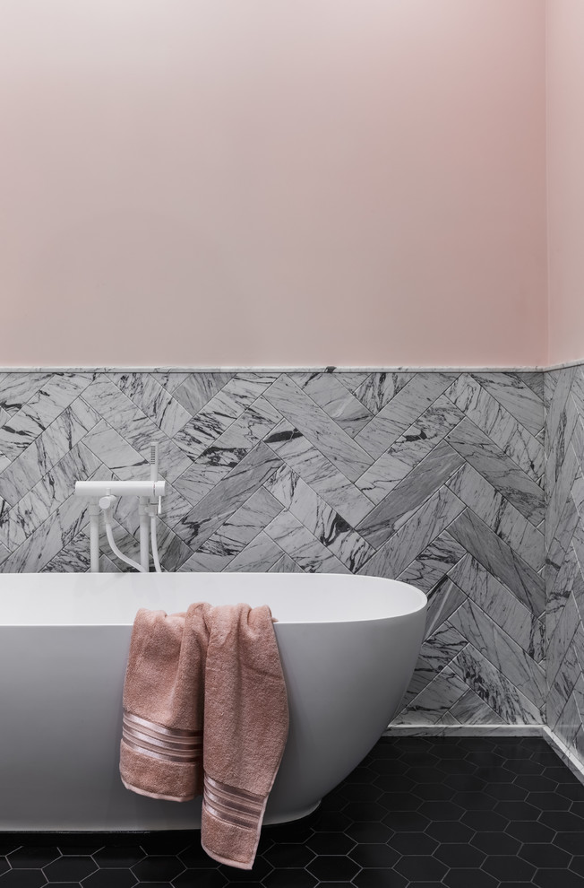 This is an example of a contemporary master bathroom in Moscow with a freestanding tub, pink walls, black floor and gray tile.