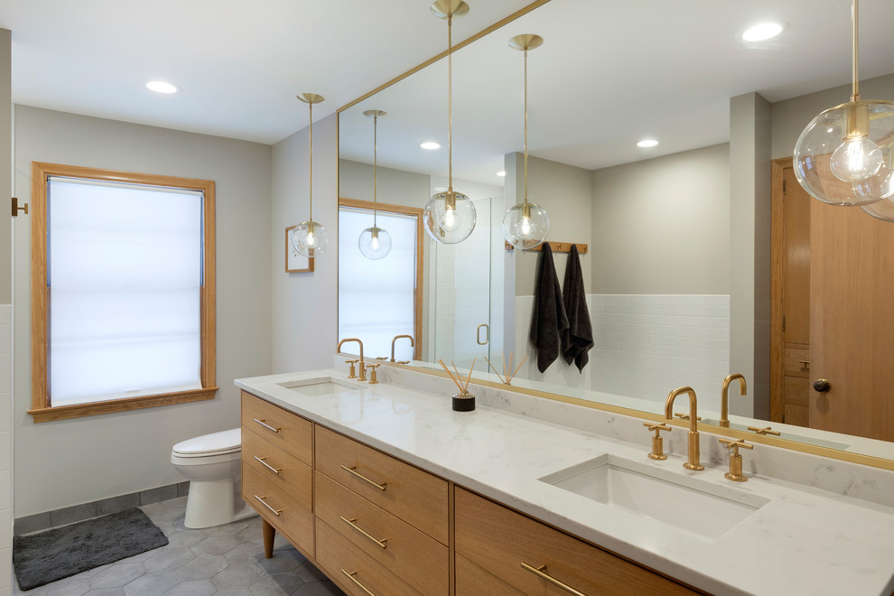 Mid-sized midcentury master bathroom in Minneapolis with furniture-like cabinets, medium wood cabinets, an alcove tub, an alcove shower, a one-piece toilet, white tile, subway tile, grey walls, porcelain floors, an undermount sink, engineered quartz benchtops, grey floor and a hinged shower door.