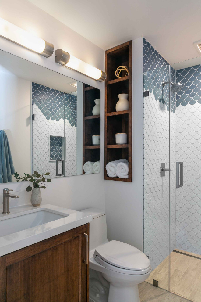 Design ideas for a transitional 3/4 bathroom in San Francisco with shaker cabinets, medium wood cabinets, an alcove shower, a one-piece toilet, blue tile, white tile, white walls, light hardwood floors, an undermount sink, brown floor, a hinged shower door and white benchtops.