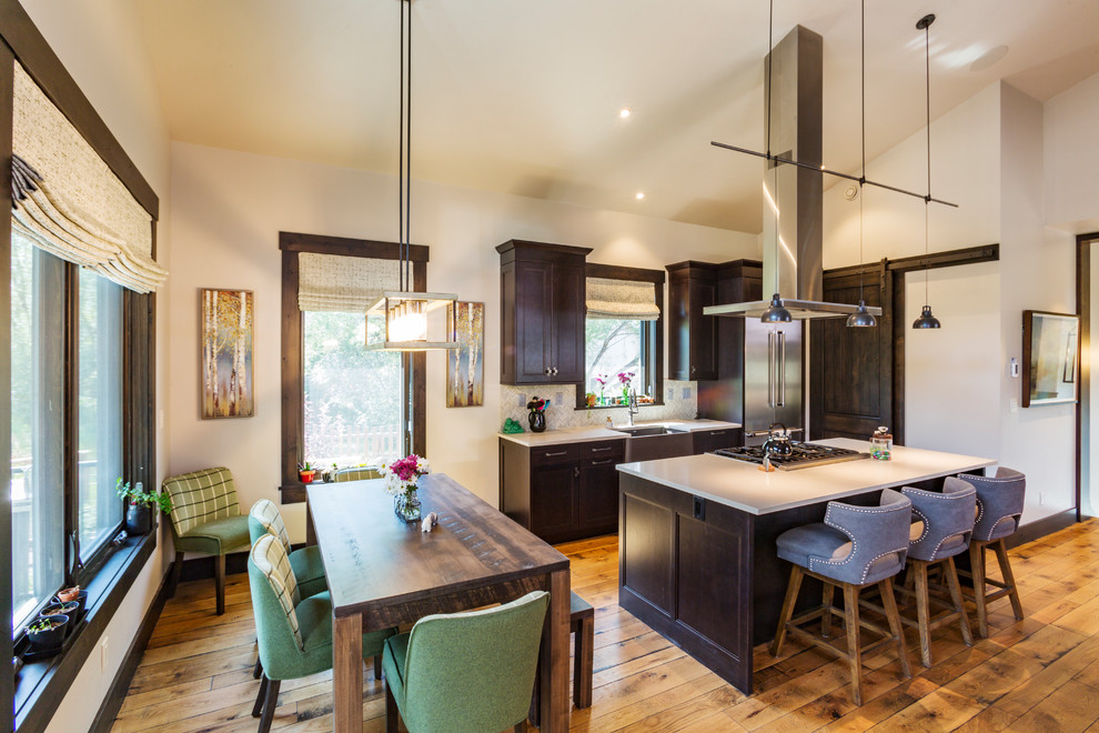 Inspiration for a transitional single-wall eat-in kitchen in Denver with a farmhouse sink, dark wood cabinets, quartz benchtops, green splashback, stone tile splashback, stainless steel appliances, medium hardwood floors, with island and white benchtop.