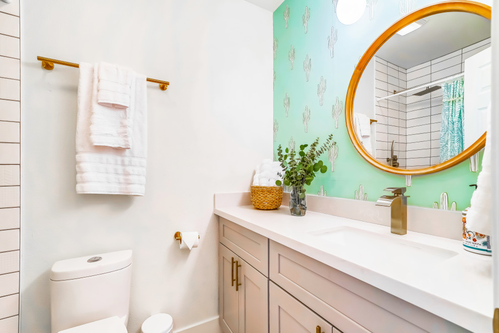 This is an example of a small contemporary kids bathroom in Phoenix with shaker cabinets, medium wood cabinets, a drop-in tub, a shower/bathtub combo, a one-piece toilet, white tile, porcelain tile, green walls, porcelain floors, an integrated sink, engineered quartz benchtops, white floor, a shower curtain, white benchtops, a single vanity, a built-in vanity, vaulted and wallpaper.
