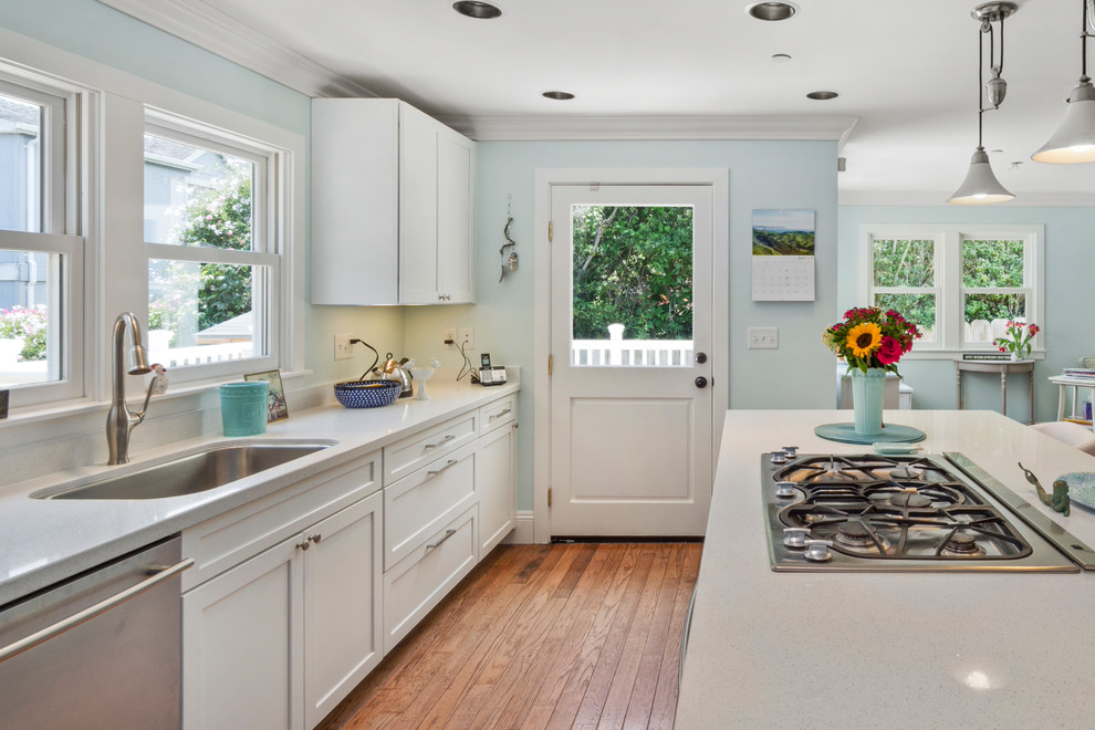Inspiration for a mid-sized beach style galley open plan kitchen in Other with a single-bowl sink, shaker cabinets, turquoise cabinets, quartz benchtops, white splashback, stainless steel appliances, medium hardwood floors, with island, brown floor and white benchtop.
