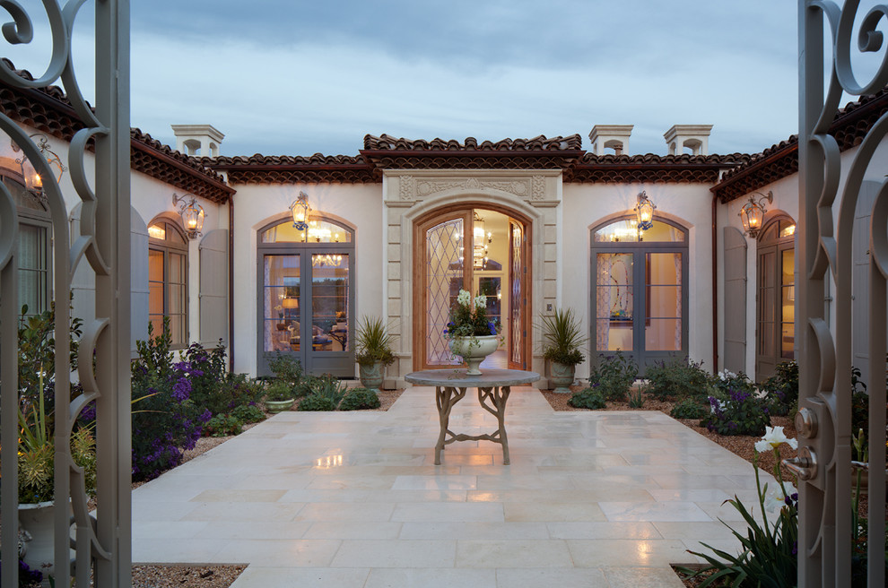 This is an example of a large mediterranean one-storey stucco beige house exterior in San Diego with a flat roof and a tile roof.