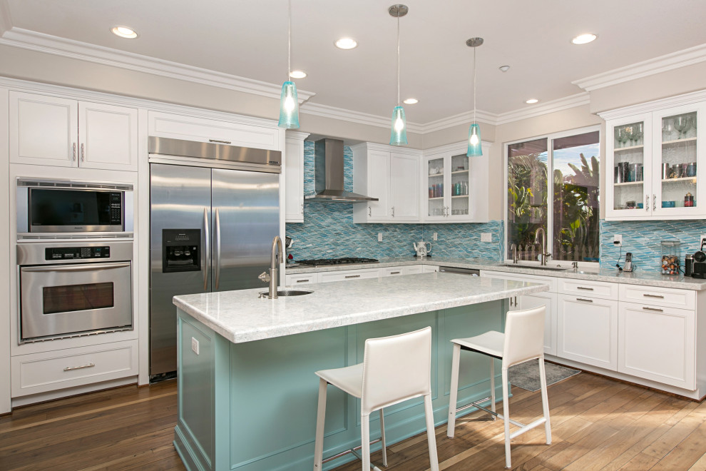 Inspiration for a large beach style l-shaped open plan kitchen in San Diego with a single-bowl sink, recessed-panel cabinets, white cabinets, quartzite benchtops, blue splashback, glass tile splashback, stainless steel appliances, medium hardwood floors, with island, brown floor and turquoise benchtop.